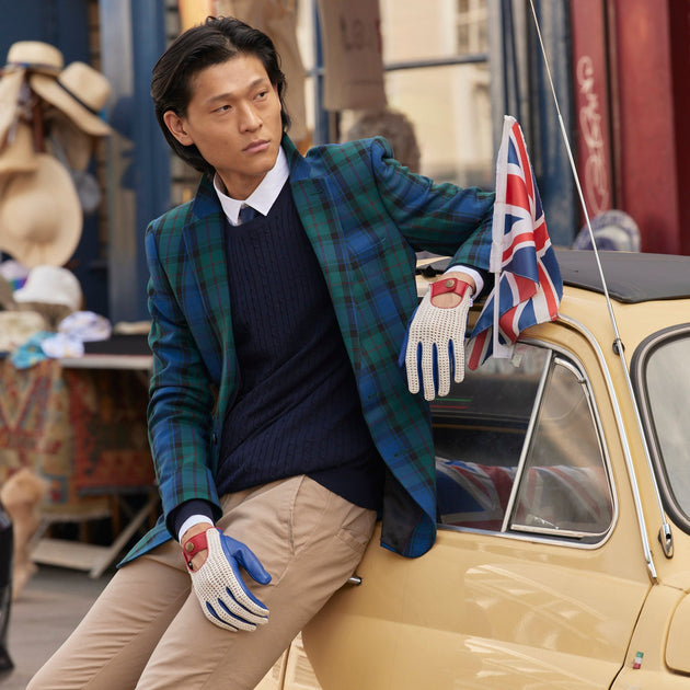 Man in Heritage Union Jack leather driving gloves holding a Union Jack flag, leaning on a vintage car in the city