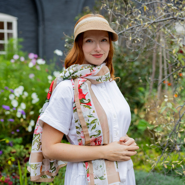 Woman wearing a floral summer scarf and straw visor in a floral garden
