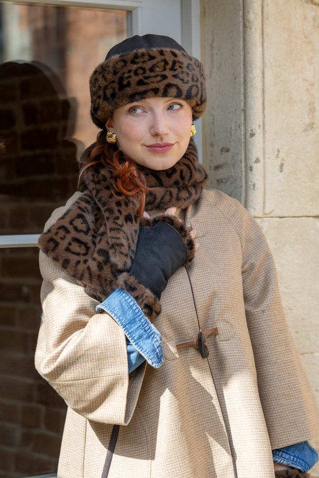 Woman wearing a hat with animal print faux fur trim and matching scarf and fingerless mittens
