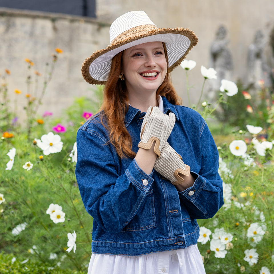 Woman wearing crochet-back leather driving gloves and a straw sun hat in a floral garden
