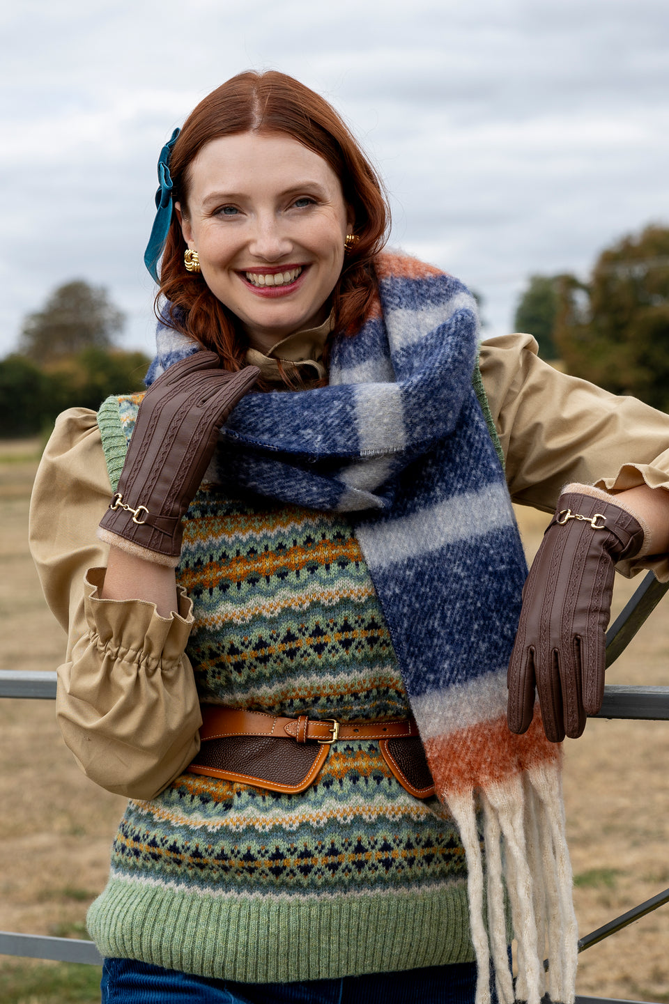 Woman wearing brown leather gloves and plaid check blanket scarf in the countryside