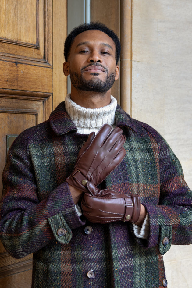 Man wearing brown leather gloves and a checked coat stood by a wooden door