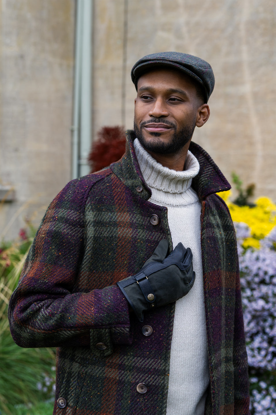 Man wearing waxed cotton and leather gloves with a tweed flat cap at a country house
