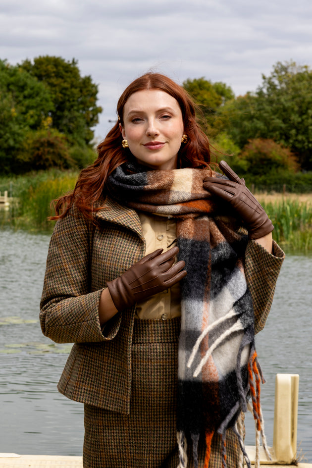 Woman wearing brown leather gloves and plaid check blanket scarf by a lake